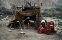 Kirghiz woman and children sitting outside tent while another woman cooks over wood fire inside.