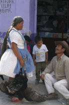 Market day.  Woman holding turkey talking to man in street with small boy.