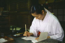 Meiji Jingu Shrine.  Japanese woman writing at desk using brush and ink.Shintu