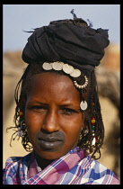 Head and shoulders portrait of Fulani woman with tattooed lips and wearing French coins in her hair.Bororo Fulbe Peul