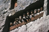 Toraja wooden funeral effigies or tau tau in cliff graves.  The figures accompany the dead from funeral house to burial ground and watch over both the living and dead.