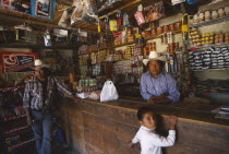 Tarahumara Indian shopkeeper and customers at wooden counter inside general stores.