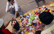 Woman buying from a pavement vendor with a display of soft toys for saleAsian Cambodian Kampuchea Southeast Asia Female Women Girl Lady Kamphuchea Female Woman Girl Lady