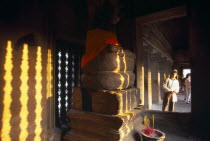 Tourist looking into interior of shrine in upper or third level with Buddha figure seated below a naga and incense offerings buring at base.