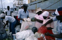 People unloading sacks of goods at port with cargo ship in background.