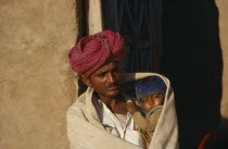 Man holding child wrapped in shawl on cold morning.