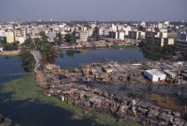 Waterside slum dwellings after fire with city buildings beyond. Dacca