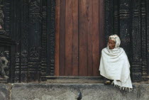 Man wrapped in white shawl sitting on the temple steps