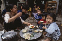 Woman and children having a meal from a tray on the pavement outside their shop
