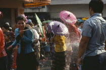 Girls with umbrellas being sprayed with water on the street during water festival.