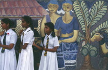 Group of school girls dressed in white standing next to mural