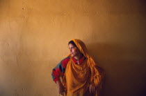 Saharawi girl standing in front of wall painted deep ochre colour. Color