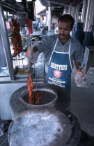 Man cooking tandoori chicken in circular clay oven at roadside stall outside Kapitan restaurant