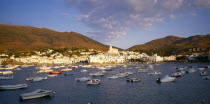 View over moored boats towards white painted town at foot of steep hillside.  Costa Brava