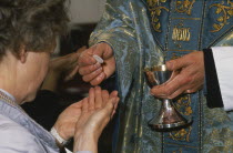 Woman holding out cupped hands to receive the host from priest during Anglican service.  Cropped view.consecrated bread or wafer