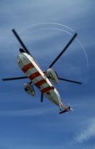 Helicopter hovering  seen from below with red and white striped undercarriage.