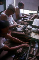 Three men rolling cigars in a small factory