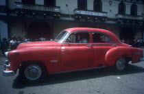 Red 1950 s car being driven in the street