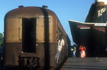 Railway carriages alongside the platform of Camaguey station with a man holding onto a carriage door with a woman walking past