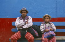 Father and Son dressed identically  sitting on a blue bench against a blue and red wall.