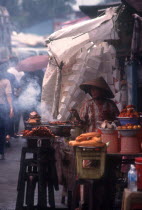Woman cooking various meat dishes at a roadside market stall.
