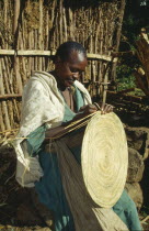 Woman making circular mat from straw  stitched into place.