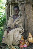 Young girl sitting in front of tree trunk with decorated gourds at her feet.