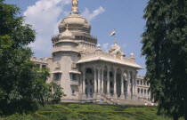 Vidhana Soudha  built in 1954 and housing the Secretariat and the State Legislature.  Exterior with domed roof and steps to colonnaded facade  part framed by trees.