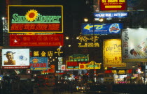 Busy street with traffic and pedestrians with neon signs and advertising illuminated at night.