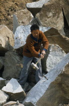 Man splitting rock in a stone quarry using a mallet and metal wedges.