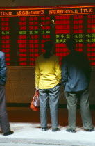 People reading stocks and shares financial information displayed in open fronted roadside building.