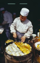 Cook turning food frying in large pan in front of him.