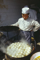 Cook lifting the lid off large dish of frying food.