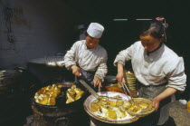 Two cooks preparing dish of fried food.