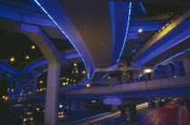 Bridge and intersecting roads seen from below  lit by ultra violet light at night with traffic light trails.