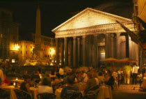 The Pantheon  exterior view at night with people eating and drinking at outside tables in the foreground.