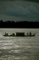 Narrow barge on the Mekong River  oarsmen silhouetted against sparkling water.