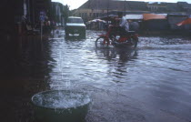 Motorcyclist driving through a flooded street.