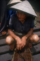 Old woman in a conical straw hat crouched on ferry deck.