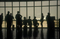 People at the airport terminal viewed from behind silhouetted against the window.