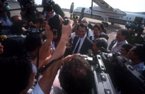 A crowd of press photographers surrounding Sonn Sen as he arrives at the airport.