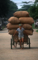 Man pulling a loaded cart stacked high with sacks behind him.