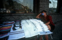 Street shirt vendor asleep beside his stall wearing a smog mask.