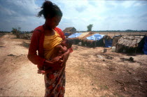 Phnom Prasat Khmer Rouge refugee camp.  Young woman breast feeding her baby  line of makeshift shelters behind.