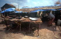 Phnom Prasat refugee camp.  Refugees in makeshift shelter with table and cooking pots in the foreground.