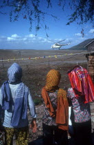 Three figures in the foreground watching a UN helicopter on the Vietnamese border.