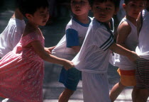 Group of young children  holding on to each other s clothing to form a line.