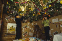 England.  Jewish children decorating the ceiling of a Sukka with cut branches and fruit during the Sukkot Festival.