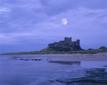 View across beach at low tide towards the castle against an early morning sky with the full moon still visible.
