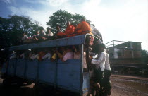 Crowded public bus  passengers sitting on roof and holding on to back as well as packed inside.